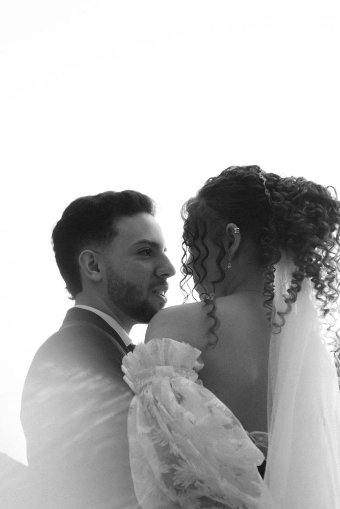 Casal abraçado em preto e branco, com véu ao vento