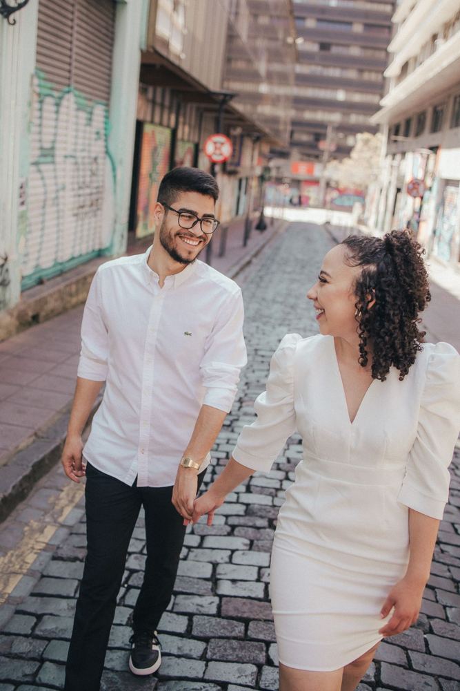 Casal de branco caminhando de mãos dadas em uma rua de paralelepípedos